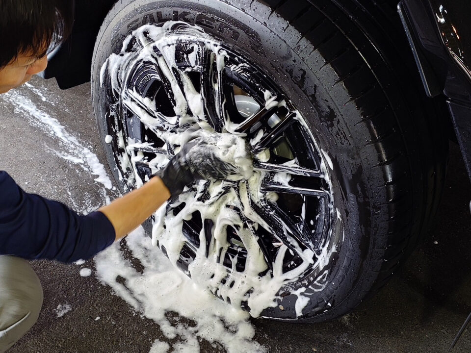 Person cleaning soapy foam off a car wheel with a dark alloy rim.