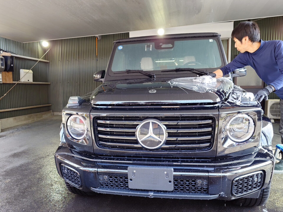 Man washing a black Mercedes-Benz G-Class SUV in a car wash bay.
