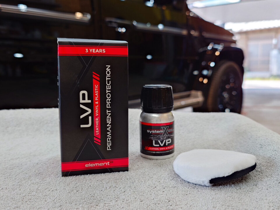 Car detailing kit on a light cloth: a black and red LVP permanent protection box, a small bottle labeled LVP, and a white applicator pad, with a dark vehicle in the background.