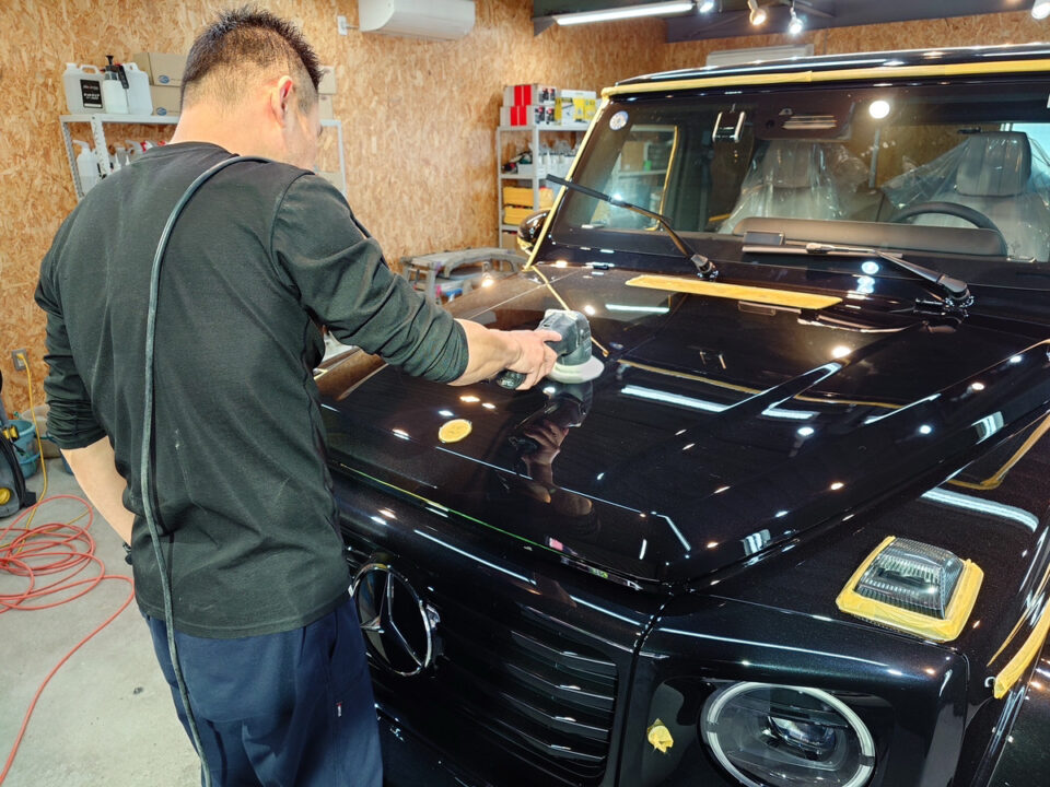 Automotive detailer buffing the hood of a glossy black SUV in a workshop.