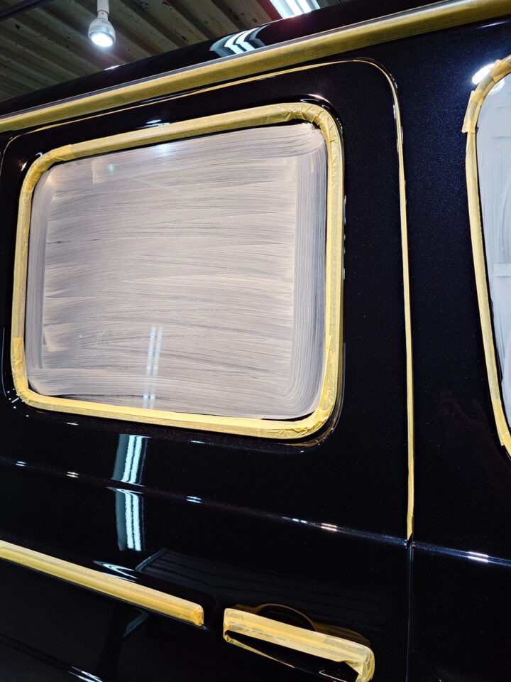 Black car door with windows masked off using painter's tape, prep for painting.