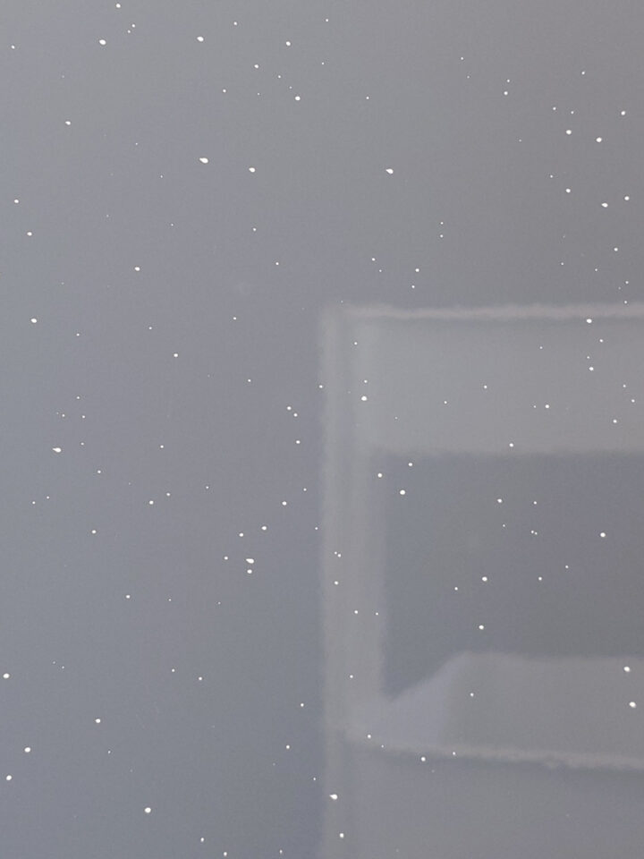 Snowflakes on a window pane with a blurred indoor reflection visible in the glass.