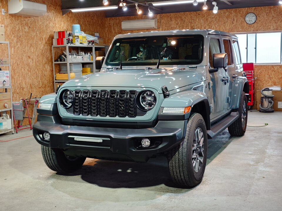 Light blue Jeep Wrangler parked inside a cluttered workshop with shelves and supplies nearby.