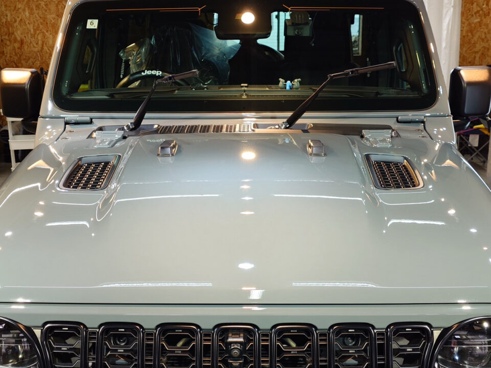 Front view of a light blue Jeep Wrangler in a showroom, showing the hood vents and seven-slot grille.
