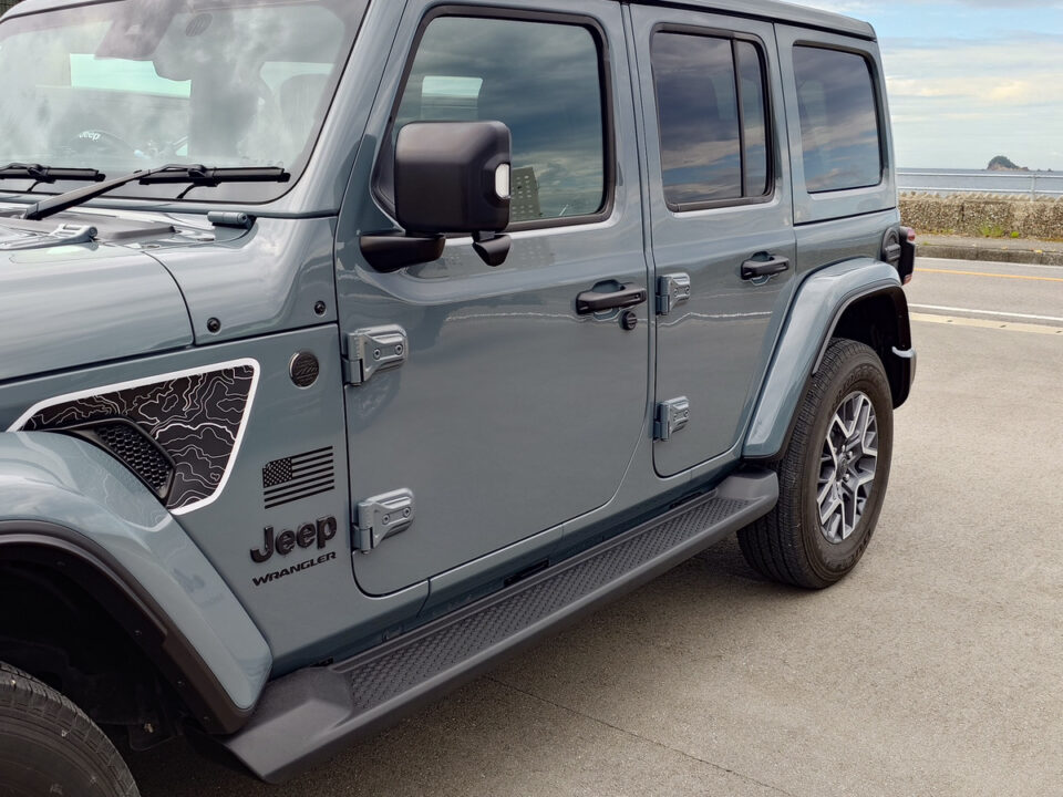 Gray Jeep Wrangler four-door SUV parked along a coastal road with the ocean in the background, side view visible.