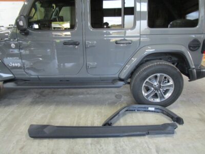 Gray Jeep Wrangler Sahara with two detached running boards/trims lying on the concrete floor beside it.