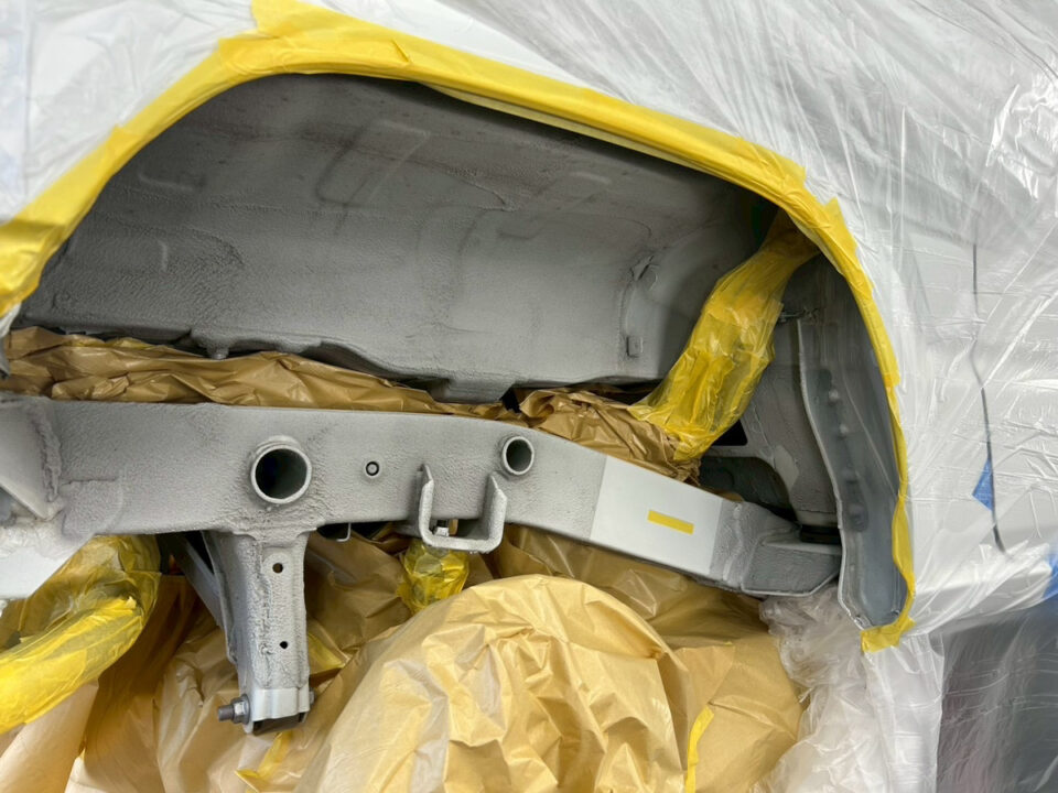 Car body panel masked for painting with yellow tape and protective plastic wrap surrounding the area.