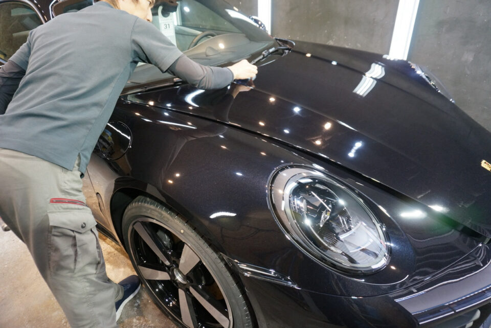 Person polishing the hood of a dark Porsche in a garage.
