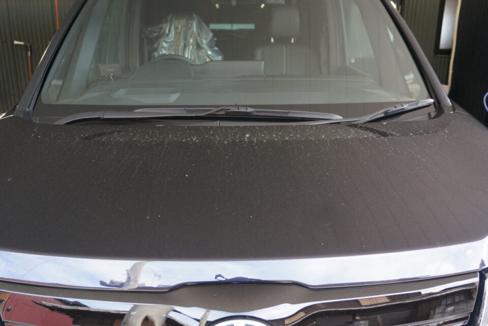 Front view of a black car hood with dust, windshield and wipers visible in a garage environment.