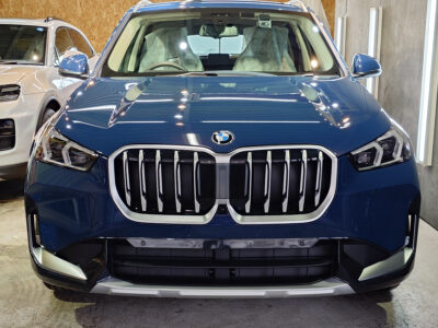 Front view of a blue BMW SUV in a showroom, highlighting the bold kidney grille and angular headlights.