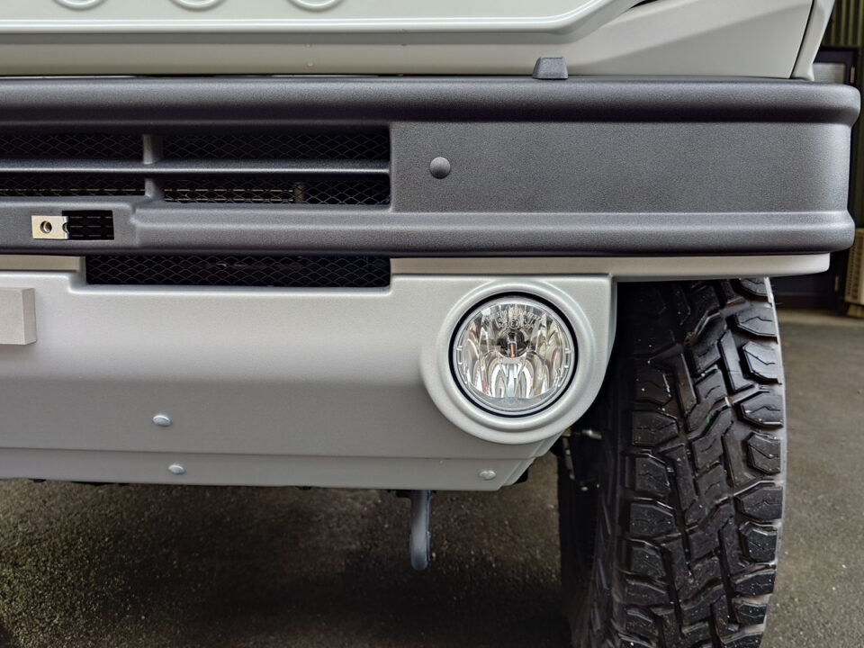 Close-up of a vehicle front bumper with a round fog light and rugged tire visible nearby.