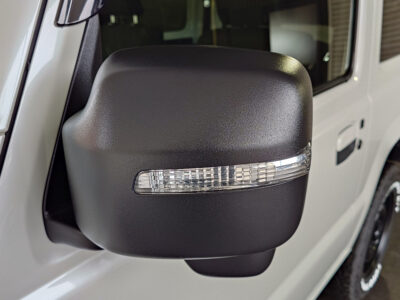 Close-up of a black side mirror on a white car, featuring a clear horizontal turn signal strip.