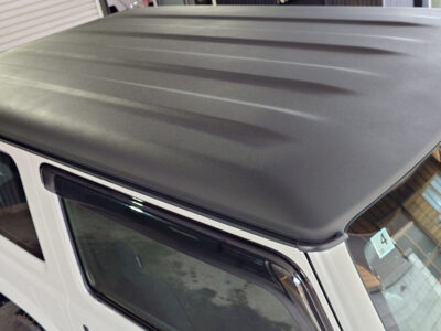 Close-up of a white SUV roof with a dark gray, ridged hardtop viewed from above, with a window and door frame visible nearby.