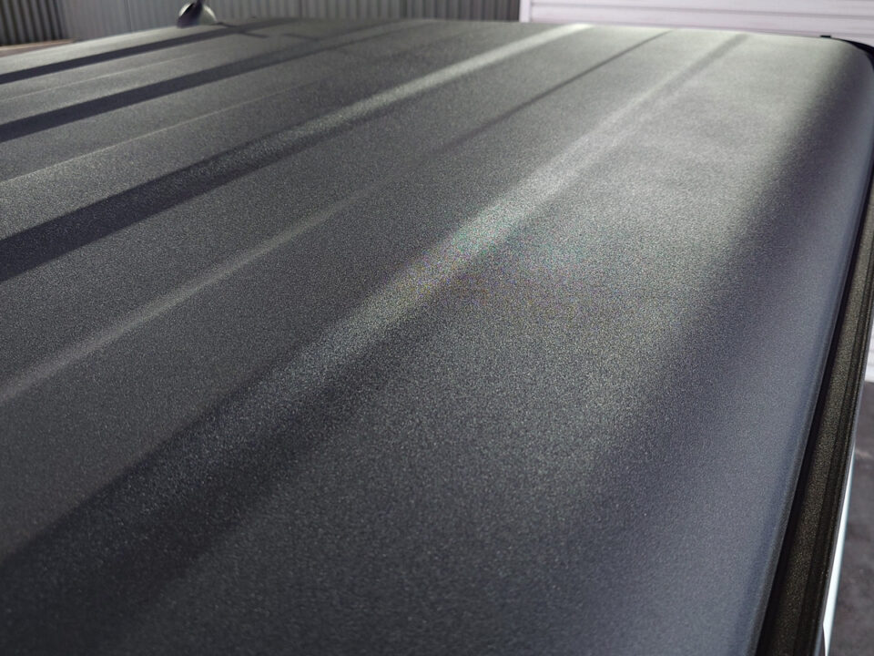 Close-up of a dark metallic car roof with fine glittery finish and light reflections amid lines along the panel