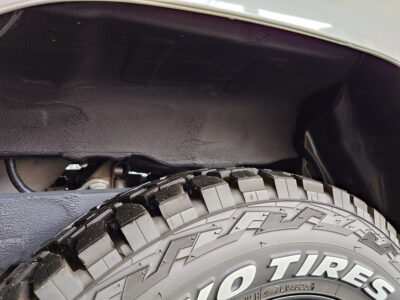 Close-up of an all-terrain tire with deep tread beside the vehicle’s wheel well.