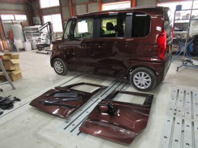 Maroon compact van in a workshop with its front and rear doors removed and laid on the floor beside it