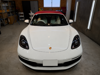 Front view of a white Porsche with a red convertible roof parked in a garage/workshop