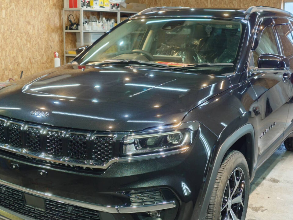 Black Jeep Grand Cherokee parked indoors in a workshop, front view with chrome grille and LED headlights.