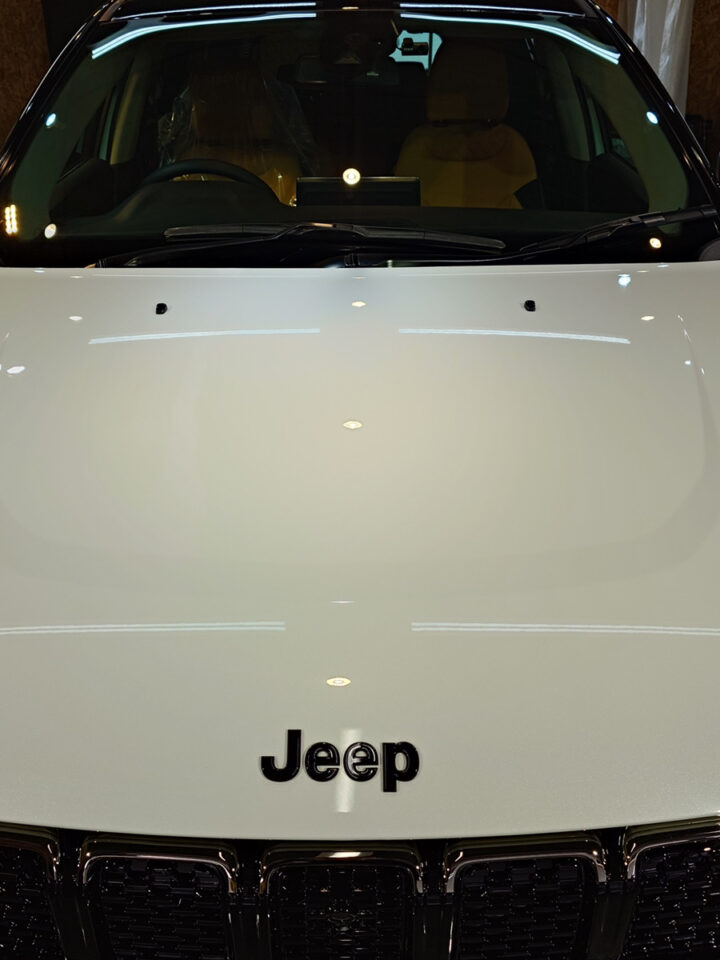 Front view of a white Jeep SUV, with the Jeep badge centered on the grille and the windshield visible above it.